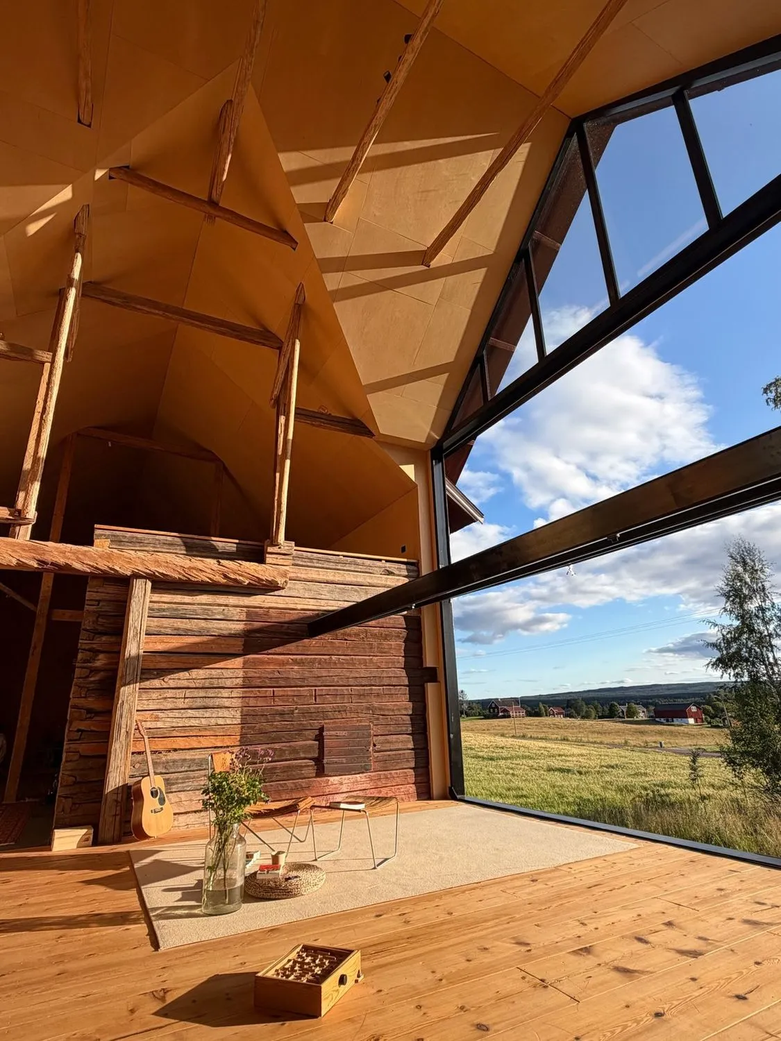 The opened window frames meadow and sky inside the timber living room