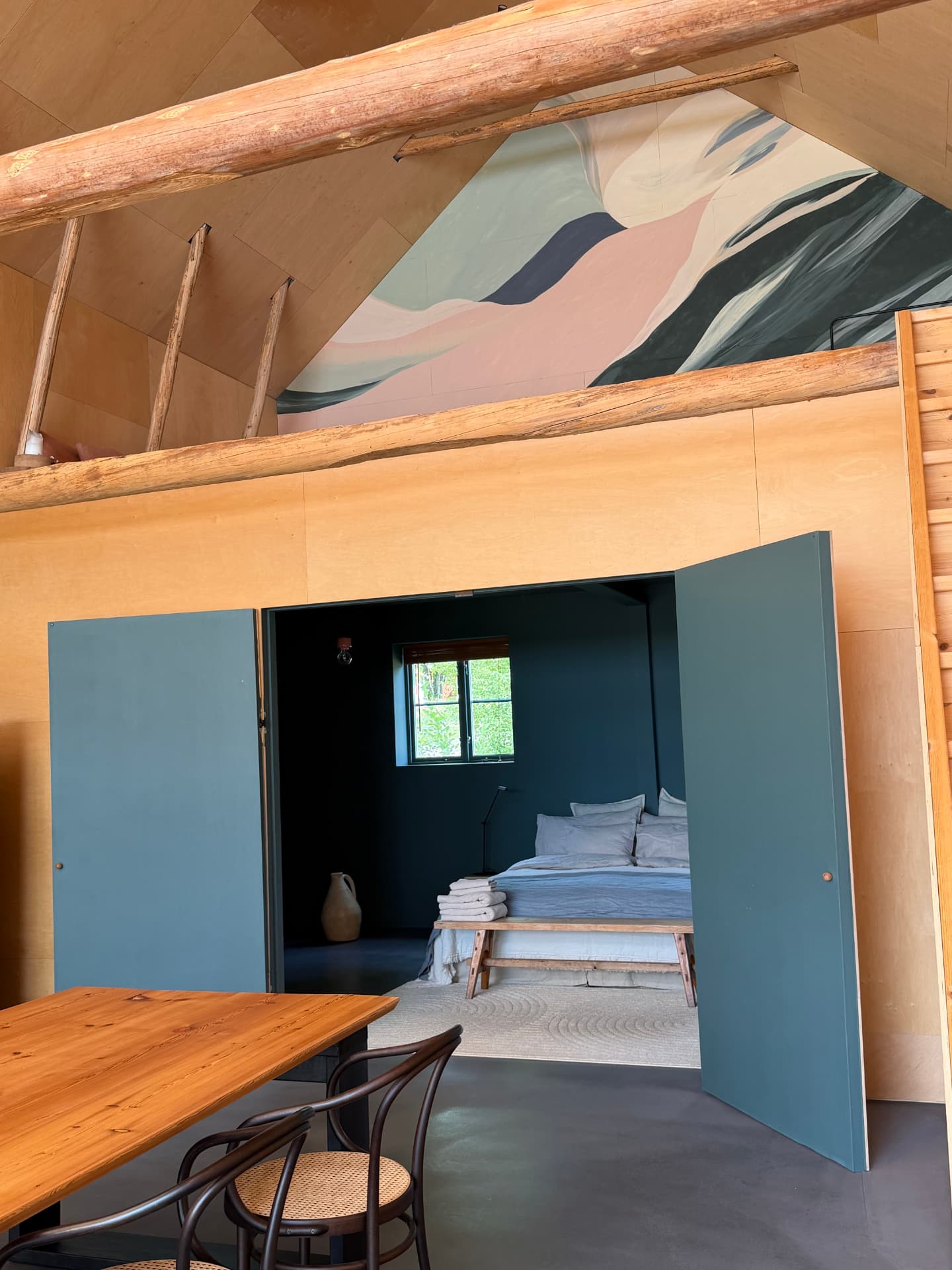 A bedroom with painted mural, blue door and open view