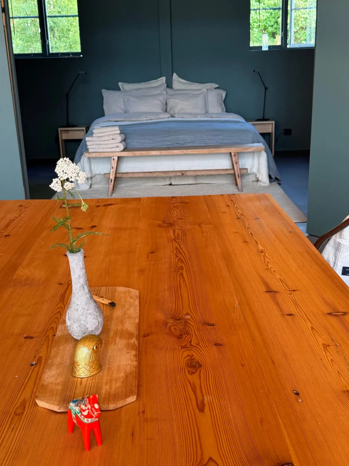 A pine table with wild flowers and a red Dala horse, a bedroom beyond