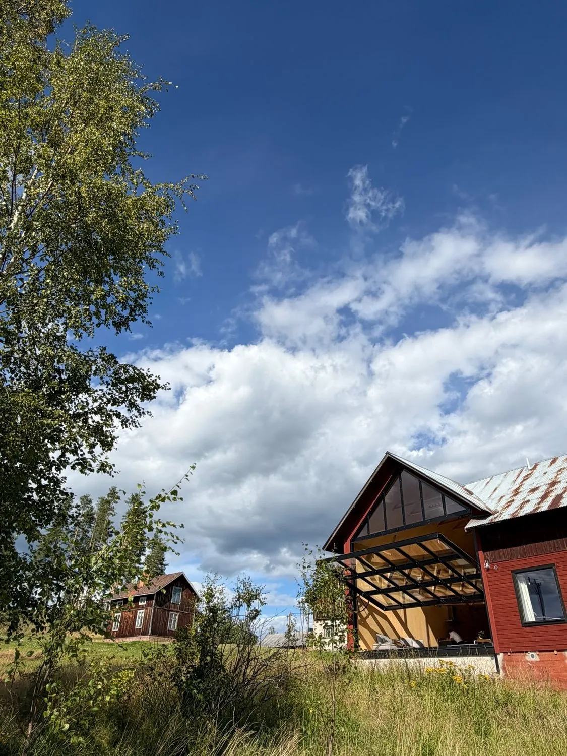 The red guesthouse with its tall glass gable under a wide Swedish sky