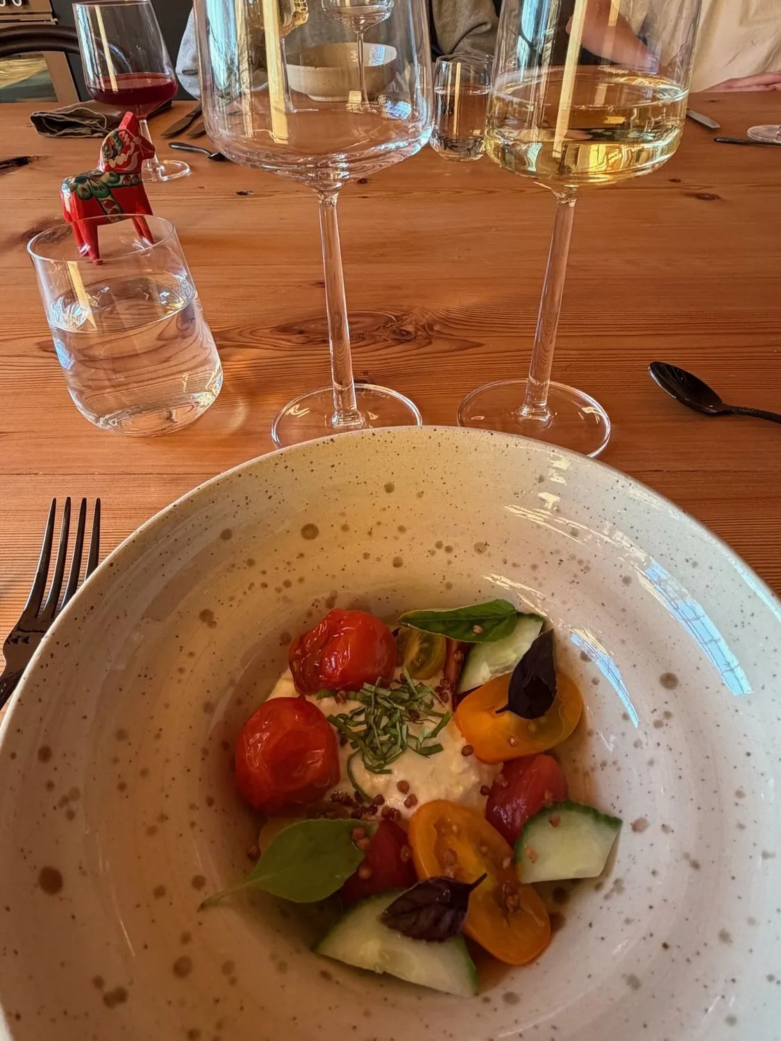 A summer plate of tomatoes and greens with wine glasses at the table