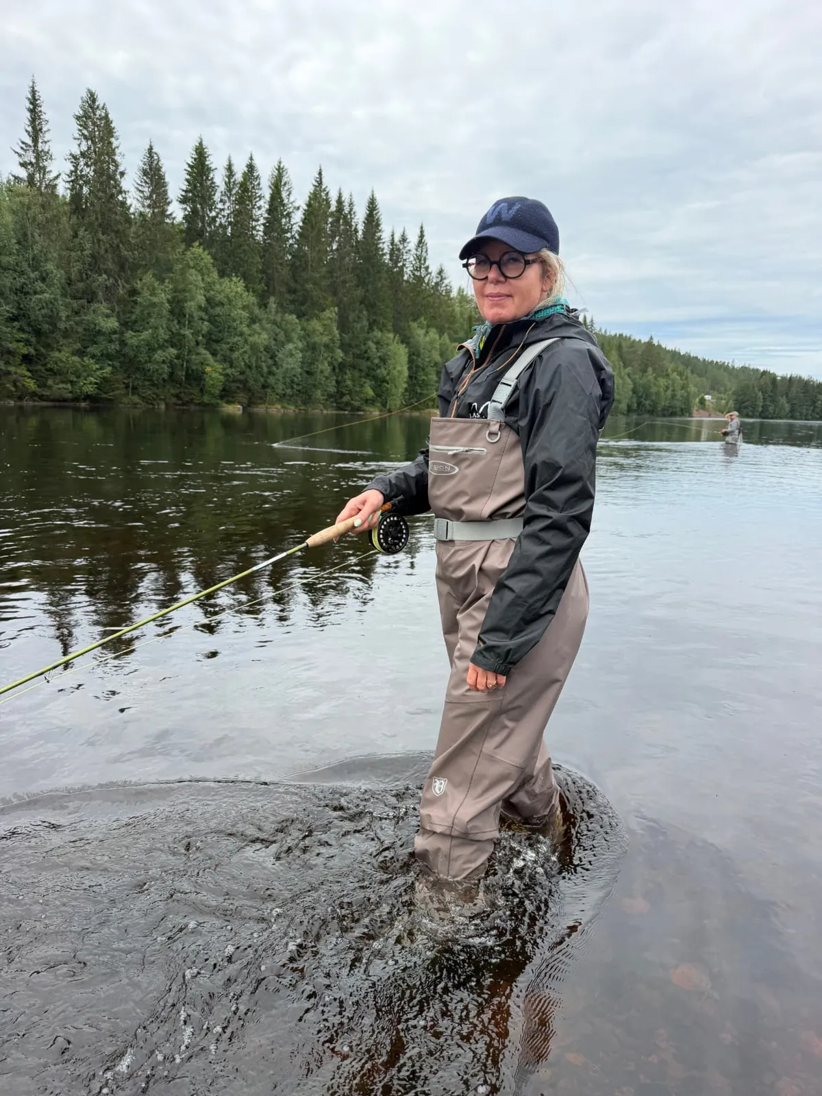 Elske fly fishing, waist-deep in a forest river