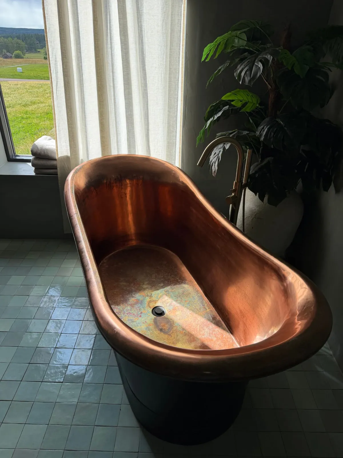 A copper bathtub beside a window onto the meadow