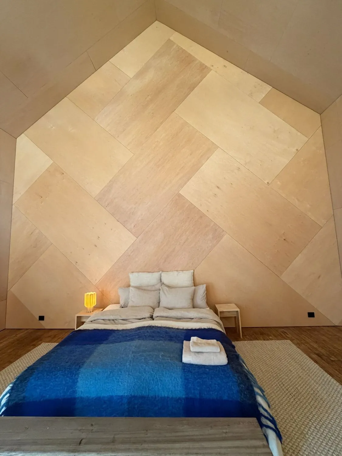 A bedroom under a herringbone timber ceiling with a deep-blue wool blanket
